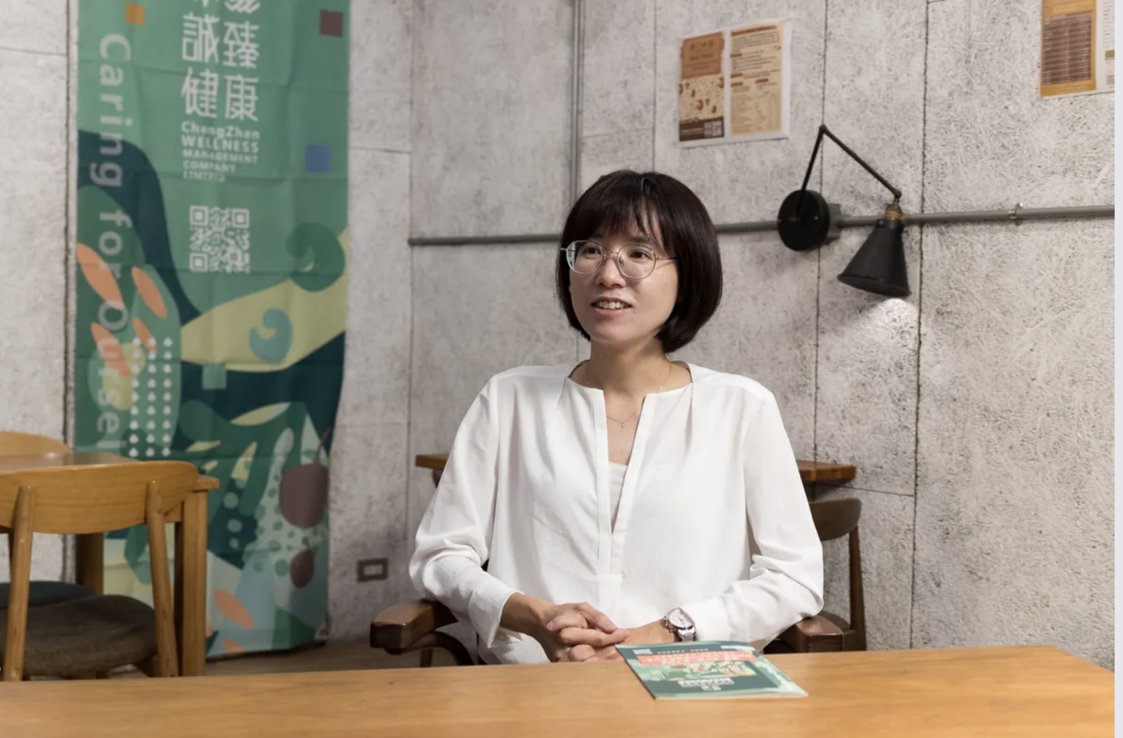 葉鈺雯在誠臻健康的品牌旗幟前受訪，坐在木桌後方說明